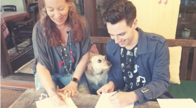 woman with red hair signing contract with young man in 20s with a dog looking up in admiration between them