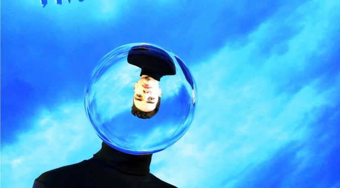 blue sky with a young man in a black polo neck jumper whos head is in a glass ball refracting.